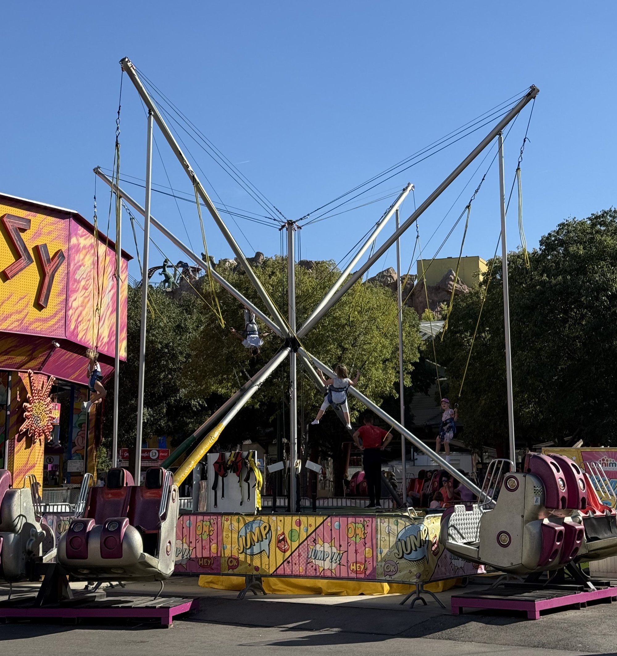 Personen die auf einem großen Trampoline, angegurtet, sehr hoch springen könnten. Tagesansicht.
